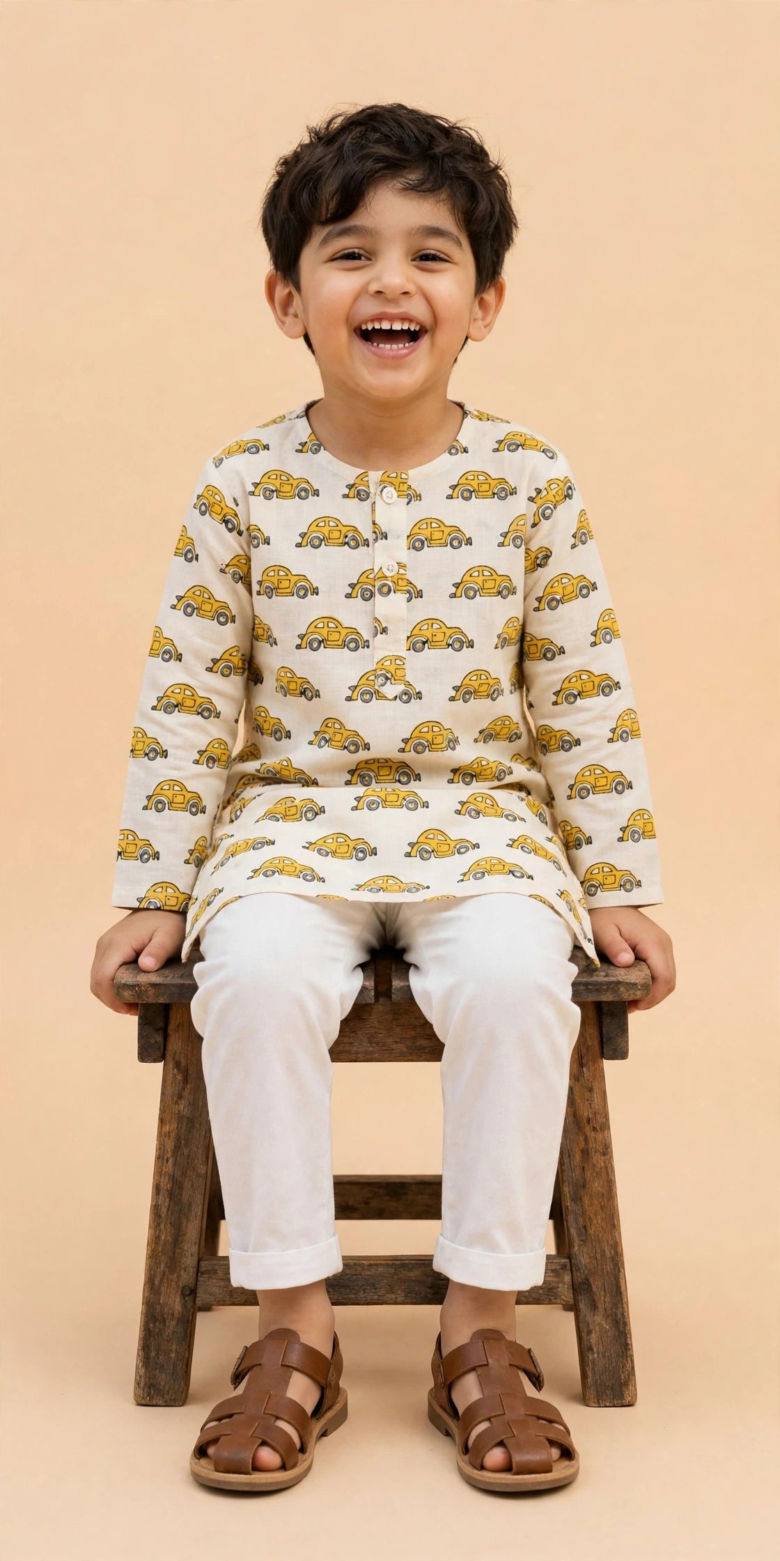 Boy seated on a stool wearing cream car print kurta and white pajama