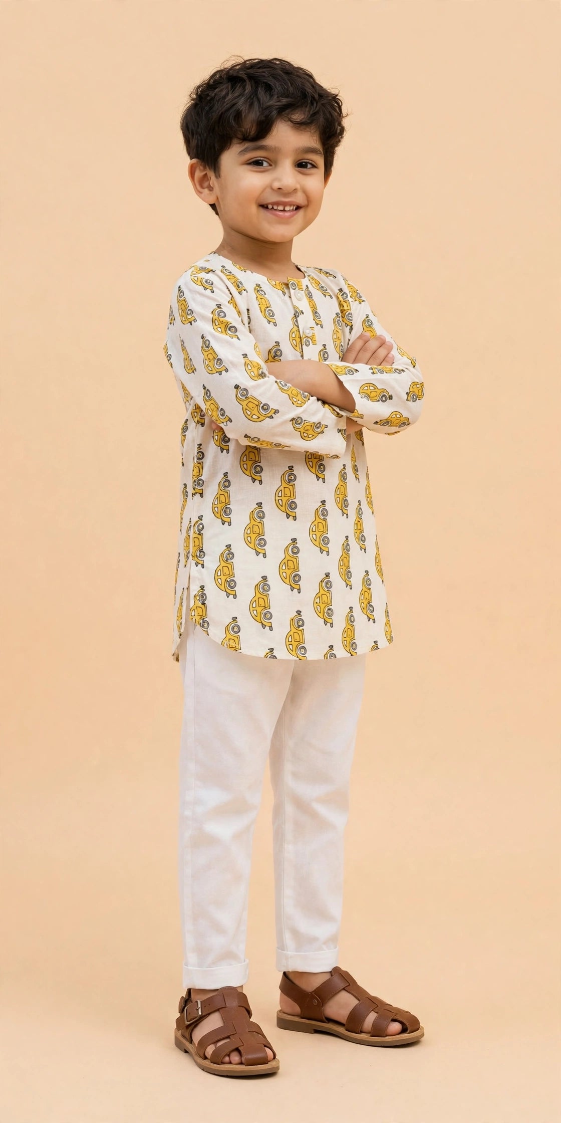 Boy sitting cross-legged in cream yellow car print kurta pajama set