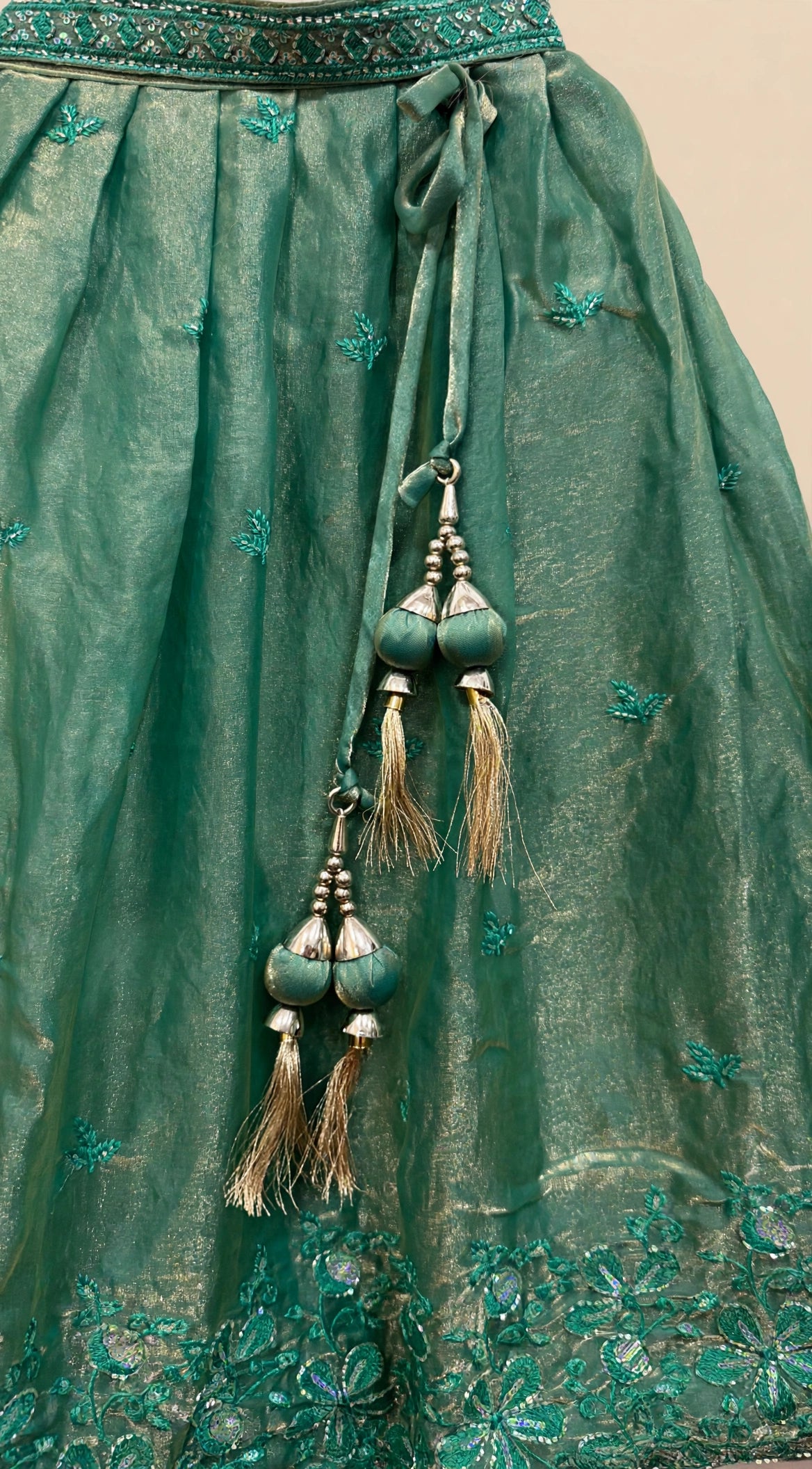 Close-up of deep green lehenga latkan with fabric balls, metallic caps, beads and gold thread tassels